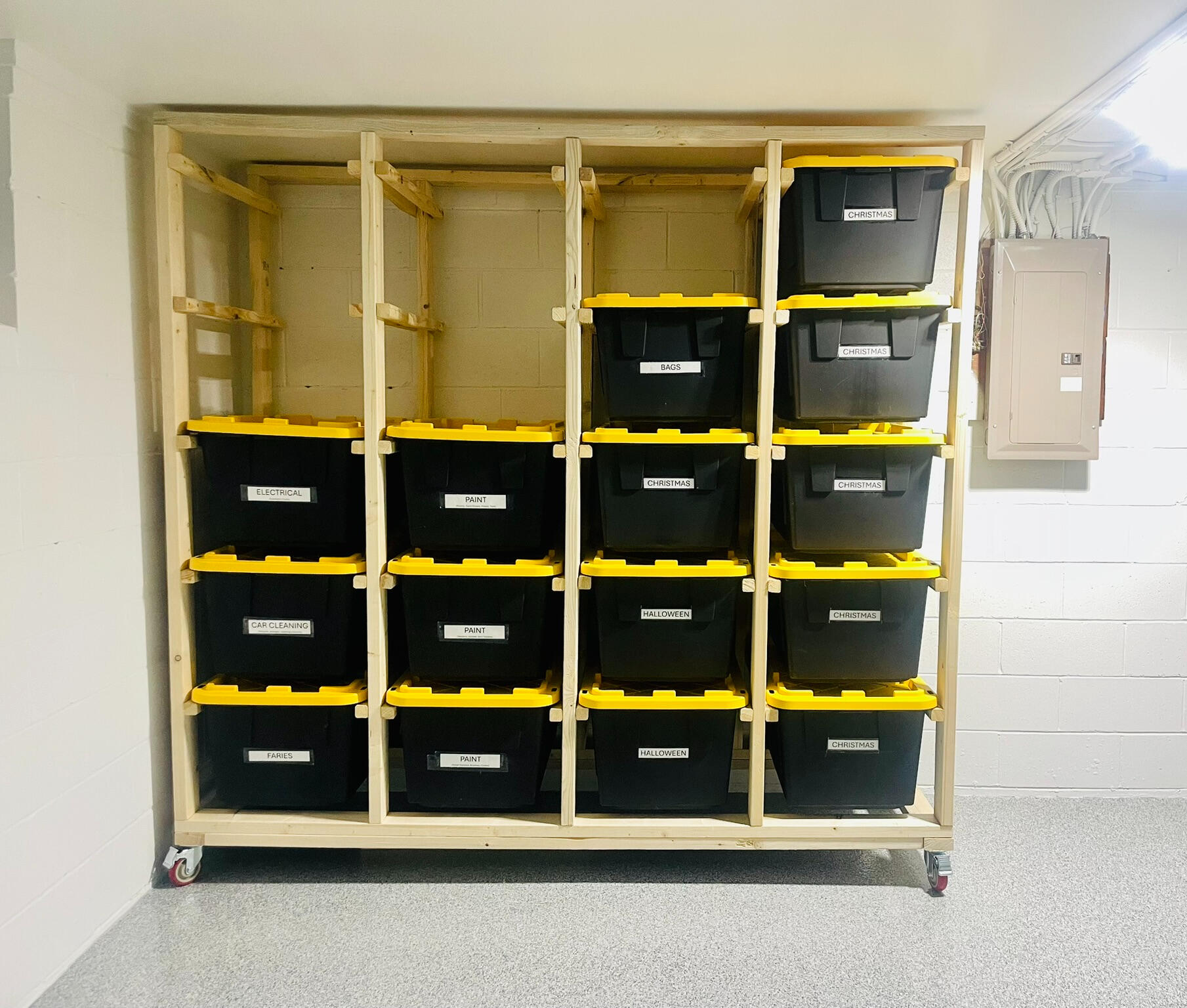 Solid wood storage system that contains 5 columns and support beams on the bottom and top. The unit is holding 20 black and yellow storage totes that are perfectly symmetrical from horizontal to vertical. The system is sitting on heavy duty casters wheels.